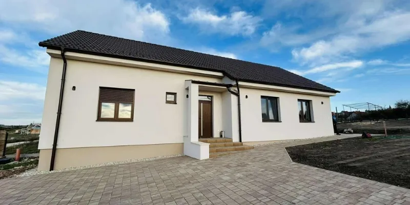 Modern, fehér homlokzatú kulcsrakész családi ház térkövezett udvarral, az RB-Bau kivitelezésében.